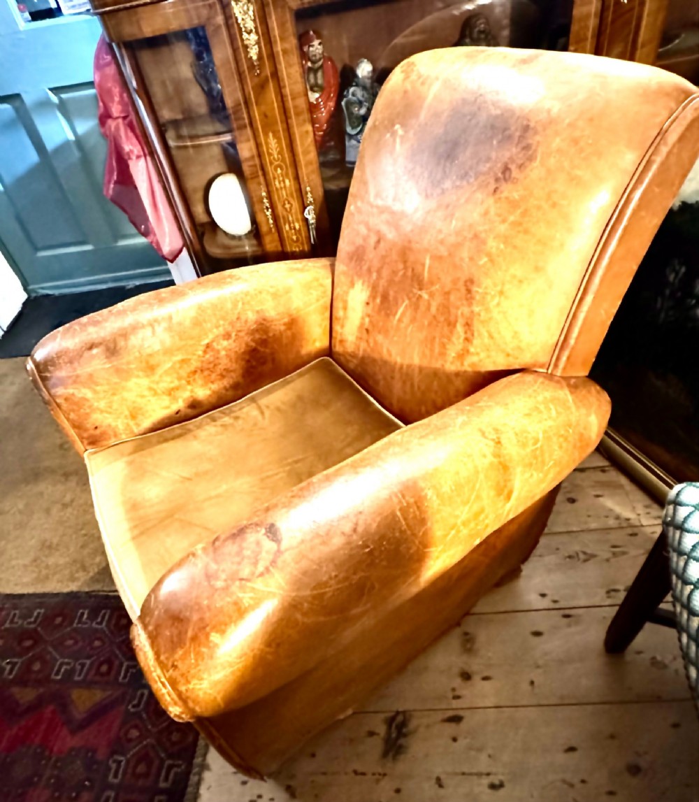 An Art Deco tan leather club chair featuring rolled armrests, distressed leather patina, and a fitted velvet seat cushion. View IV