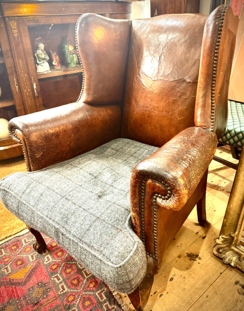A late 19th-century Victorian wingback armchair upholstered in aged tan leather with brass studding and a textured grey tweed seat cushion.