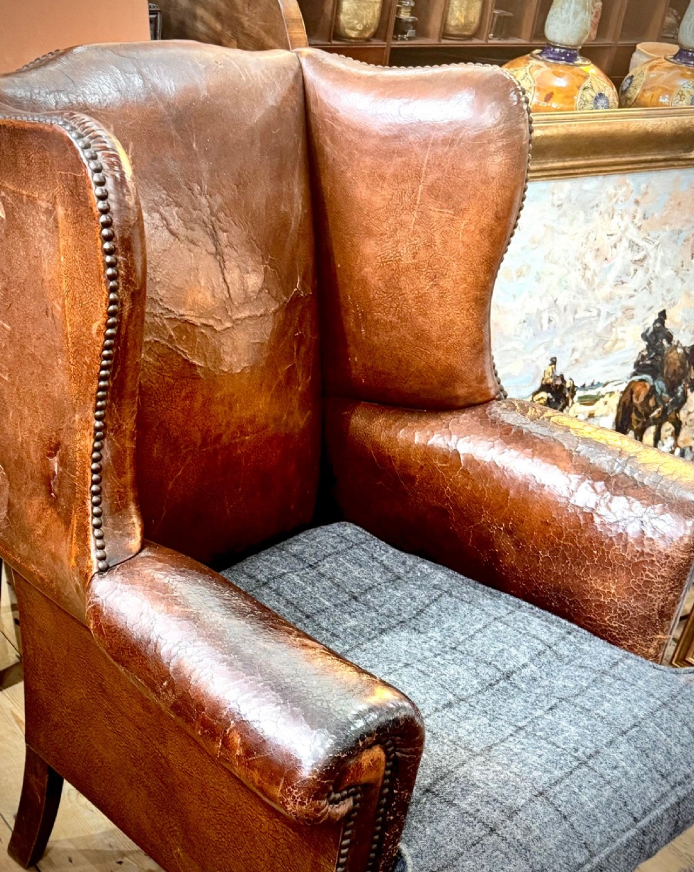 A late 19th-century Victorian wingback armchair upholstered in aged tan leather with brass studding and a textured grey tweed seat cushion. View II