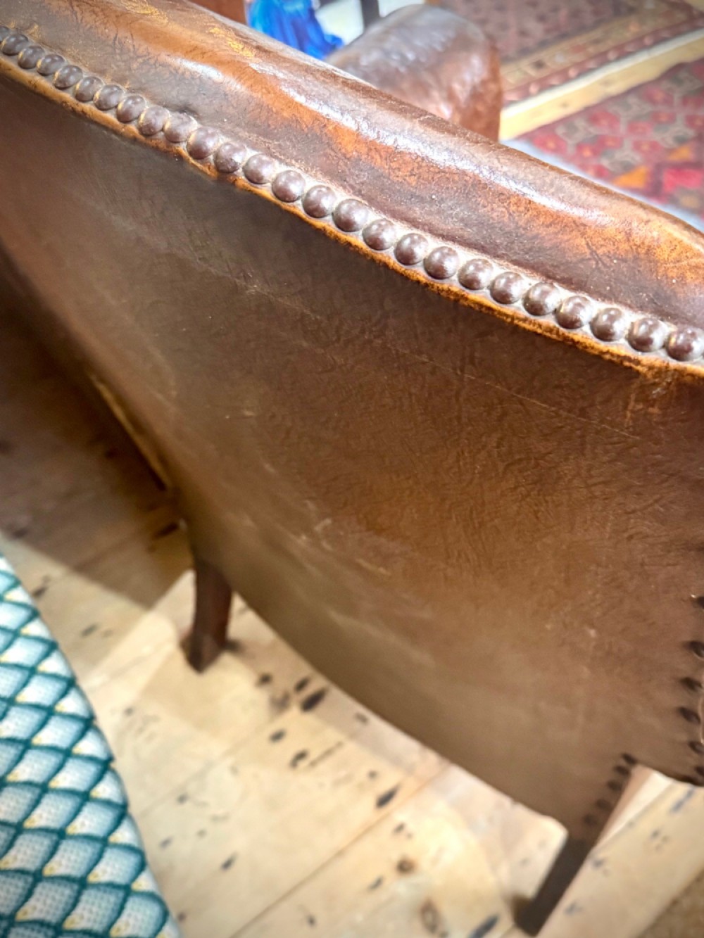 A late 19th-century Victorian wingback armchair upholstered in aged tan leather with brass studding and a textured grey tweed seat cushion. View V