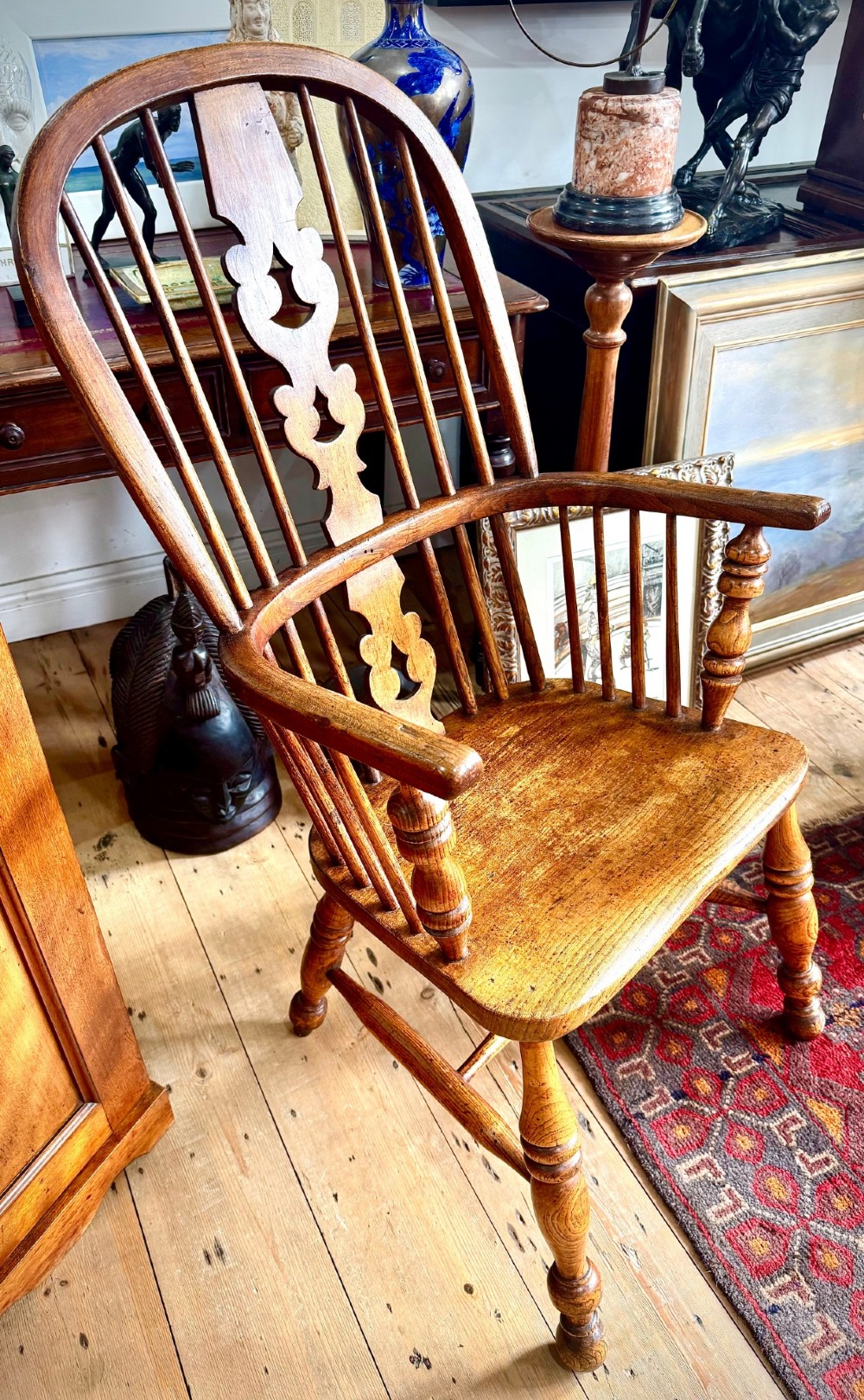 A 19th-century high-back Windsor armchair featuring a steam-bent hoop back, pierced central splat, shaped elm seat, and turned wooden legs.