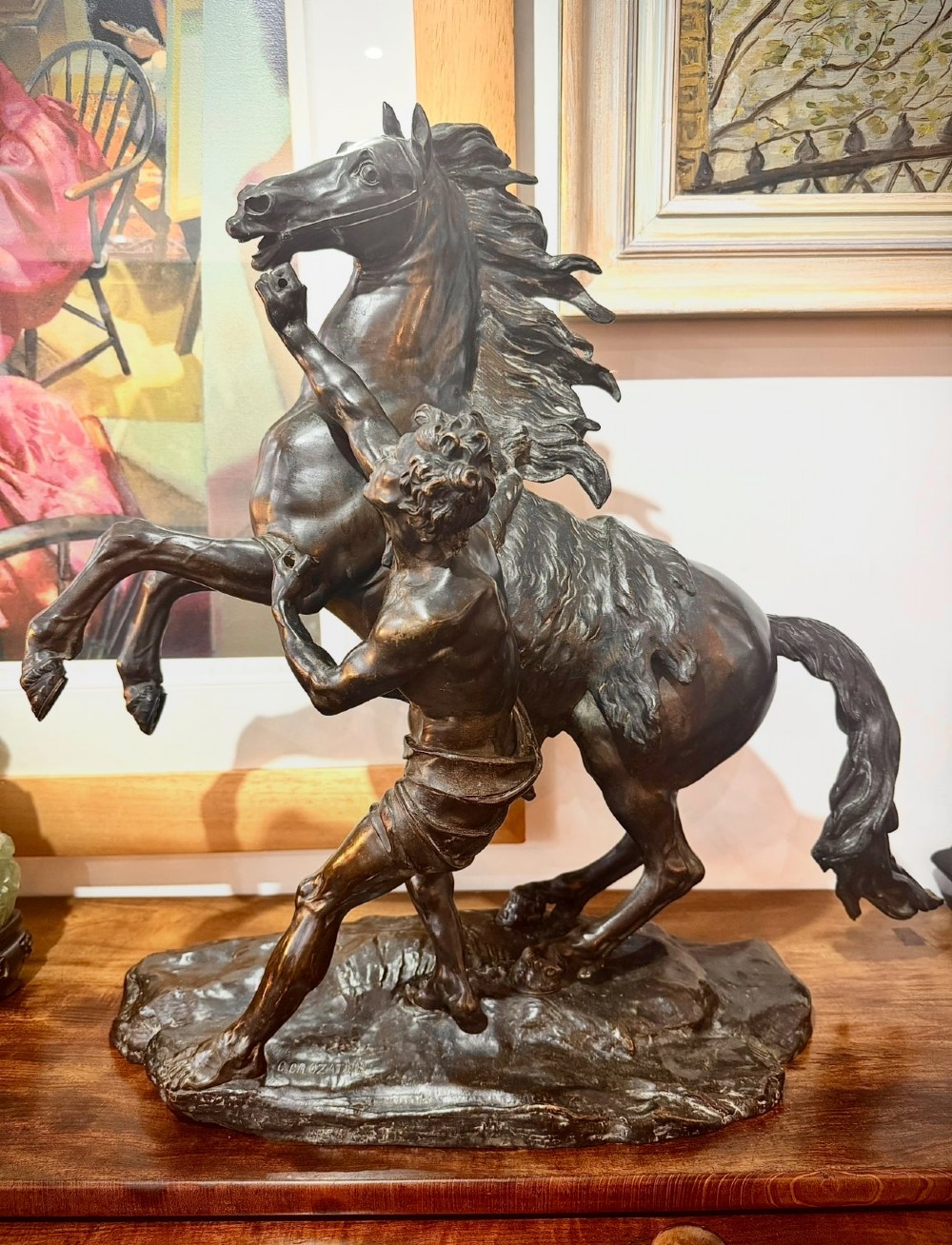 A dark patinated bronze sculpture depicting a rearing horse restrained by a groom, mounted on a naturalistic rocky base.