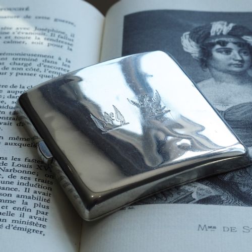 fig 3. A polished Victorian sterling silver cigarette case featuring an engraved heraldic crest and curved profile resting on an open book.