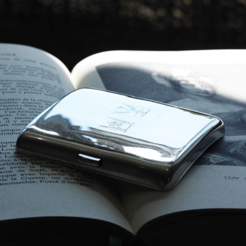 fig 6. A polished Victorian sterling silver cigarette case featuring an engraved heraldic crest and curved profile resting on an open book.