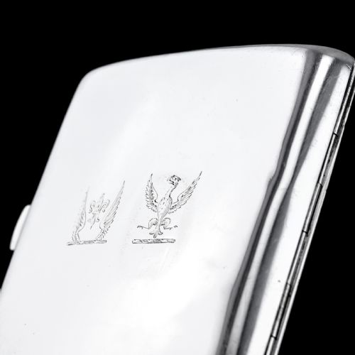 fig 9. A polished Victorian sterling silver cigarette case featuring an engraved heraldic crest and curved profile resting on an open book.