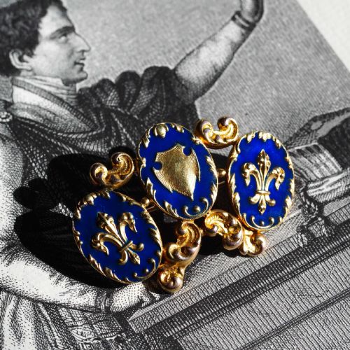 fig 5. A 19th-century 18ct gold brooch featuring three dark blue enamel oval cartouches decorated with gold heraldic motifs and rococo scrollwork.