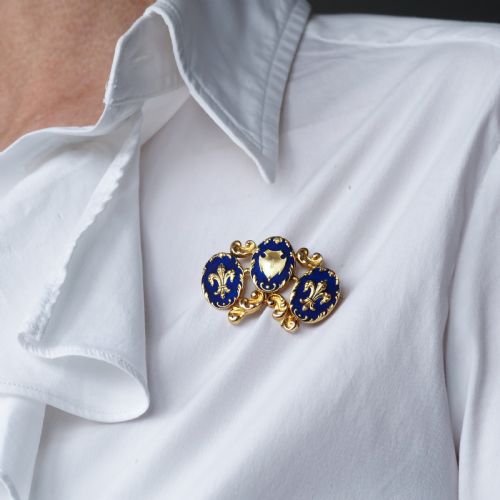 fig 7. A 19th-century 18ct gold brooch featuring three dark blue enamel oval cartouches decorated with gold heraldic motifs and rococo scrollwork.