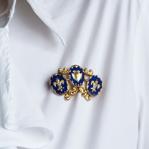fig 8. A 19th-century 18ct gold brooch featuring three dark blue enamel oval cartouches decorated with gold heraldic motifs and rococo scrollwork.