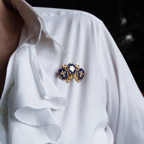 fig 9. A 19th-century 18ct gold brooch featuring three dark blue enamel oval cartouches decorated with gold heraldic motifs and rococo scrollwork.