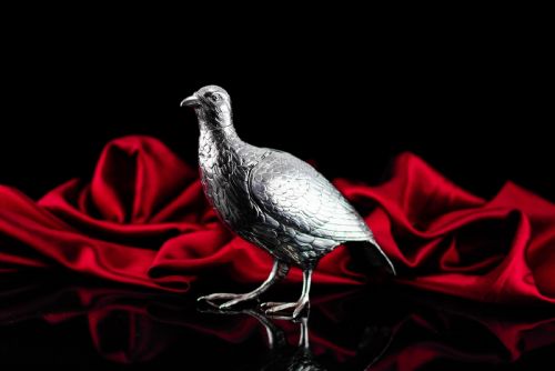 fig 1. A solid silver model of a partridge with chased feather detailing standing on two feet with a hinged compartment lid along its back.