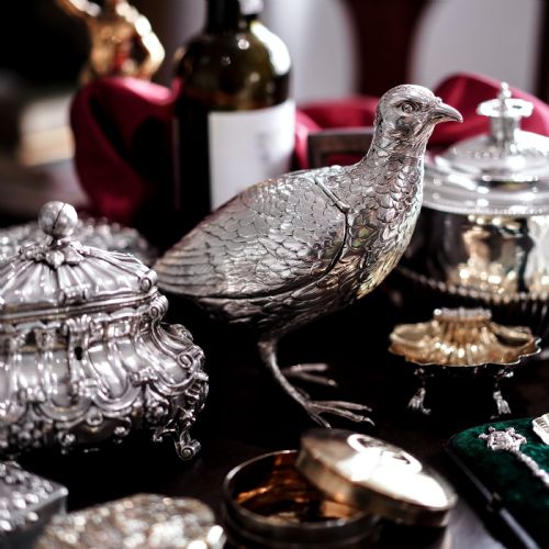 fig 7. A solid silver model of a partridge with chased feather detailing standing on two feet with a hinged compartment lid along its back.