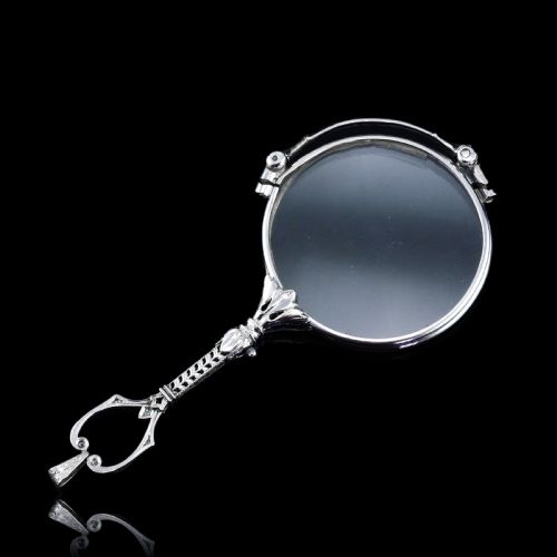 fig 1. An Art Deco platinum lorgnette featuring a circular folding magnifying glass lens attached to a geometric handle set with small diamonds.