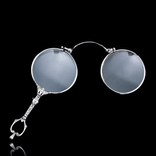 fig 2. An Art Deco platinum lorgnette featuring a circular folding magnifying glass lens attached to a geometric handle set with small diamonds.