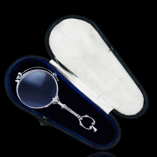 fig 3. An Art Deco platinum lorgnette featuring a circular folding magnifying glass lens attached to a geometric handle set with small diamonds.