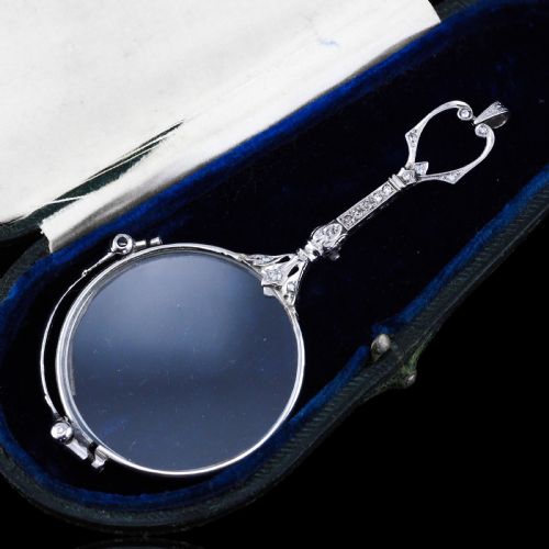 fig 4. An Art Deco platinum lorgnette featuring a circular folding magnifying glass lens attached to a geometric handle set with small diamonds.