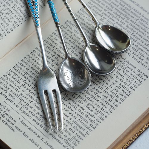 fig 7. A four-piece set of late 19th-century Russian silver and cloisonne enamel cutlery featuring three spoons and a fork with turquoise blue, white, and red floral motifs.