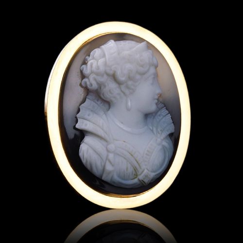 fig 1. An oval Victorian hardstone agate cameo featuring a white relief carved portrait of a woman against a dark background, set in a plain 18ct gold bezel frame.