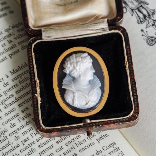 fig 2. An oval Victorian hardstone agate cameo featuring a white relief carved portrait of a woman against a dark background, set in a plain 18ct gold bezel frame.