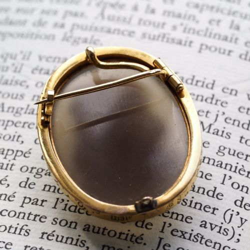 fig 7. An oval Victorian hardstone agate cameo featuring a white relief carved portrait of a woman against a dark background, set in a plain 18ct gold bezel frame.