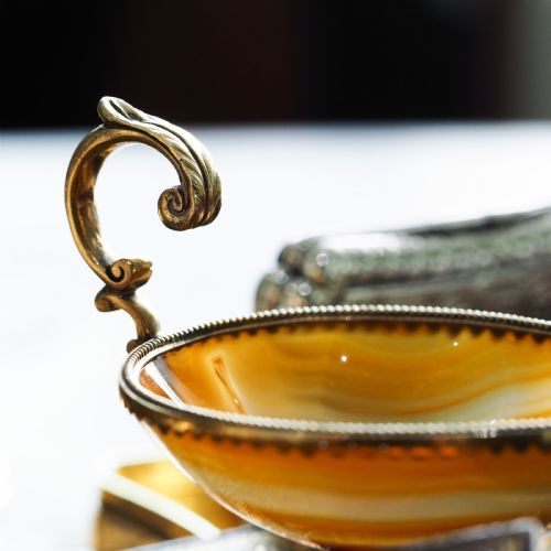 fig 1. A 19th-century carved brown banded agate cup featuring a silver-gilt rim, pedestal base, and an ornate scroll handle.