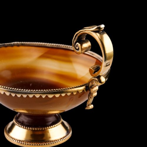 fig 4. A 19th-century carved brown banded agate cup featuring a silver-gilt rim, pedestal base, and an ornate scroll handle.