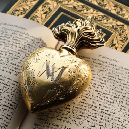 fig 5. A 19th-century French silver-gilt heart-shaped scent bottle featuring an engraved monogram, foliate scrollwork, and a flame-shaped stopper.