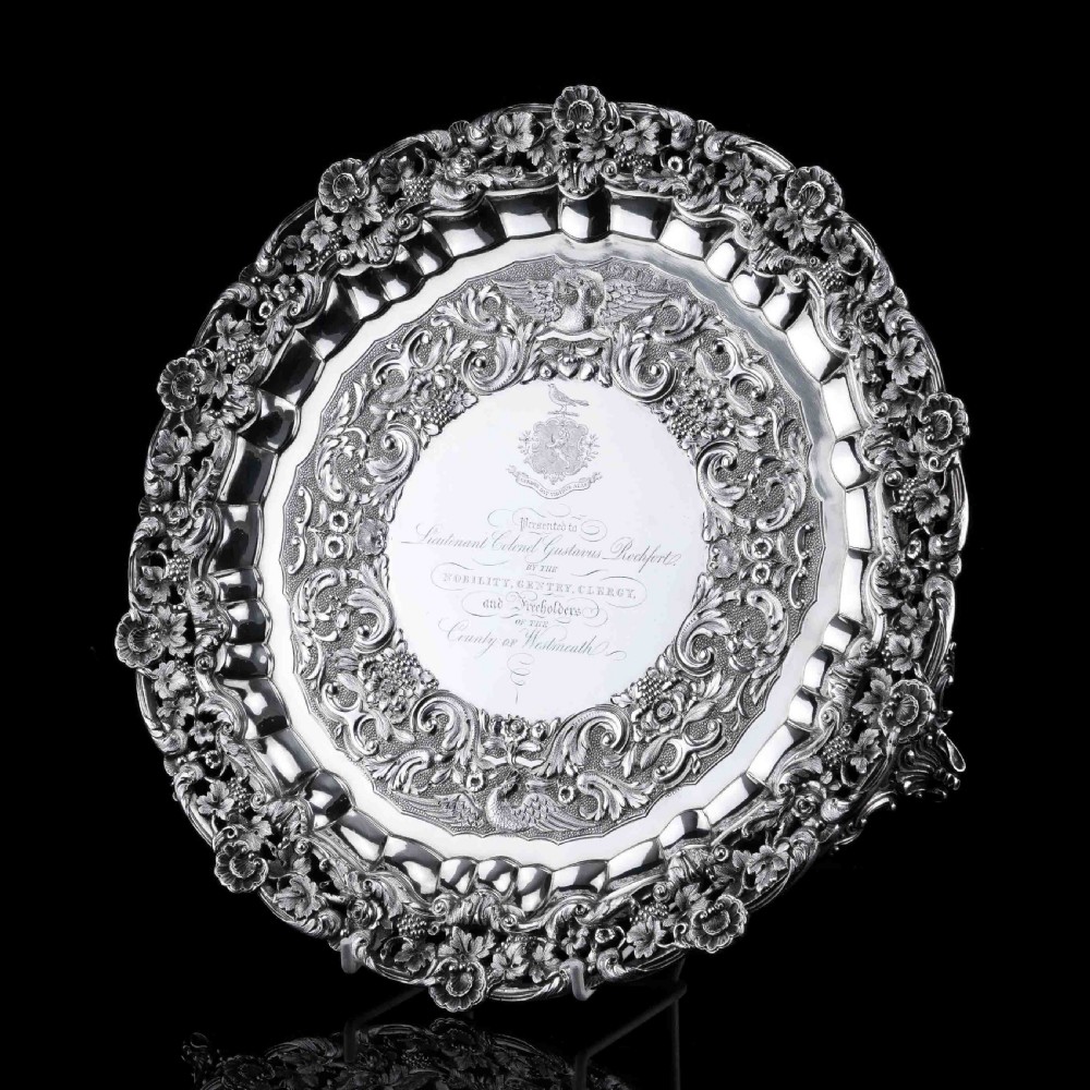A circular Georgian sterling silver salver featuring an intricately detailed cast floral border and central inscription engraving. View X