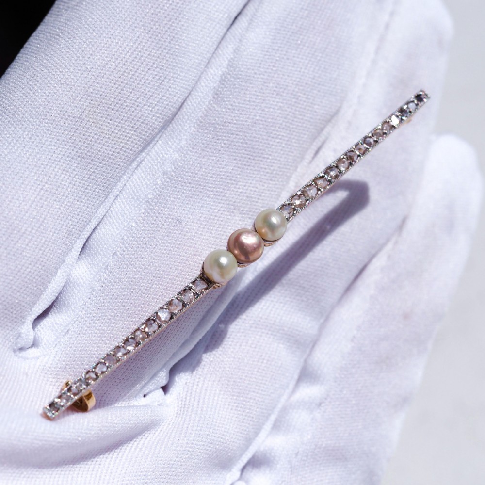 An antique platinum and gold linear bar brooch set with diamonds and three central pearls, featuring a soft pink pearl in the centre. View V