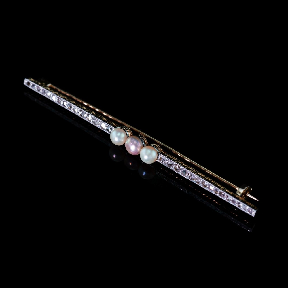 An antique platinum and gold linear bar brooch set with diamonds and three central pearls, featuring a soft pink pearl in the centre. View IV