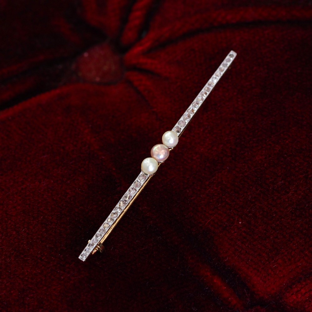 An antique platinum and gold linear bar brooch set with diamonds and three central pearls, featuring a soft pink pearl in the centre. View X