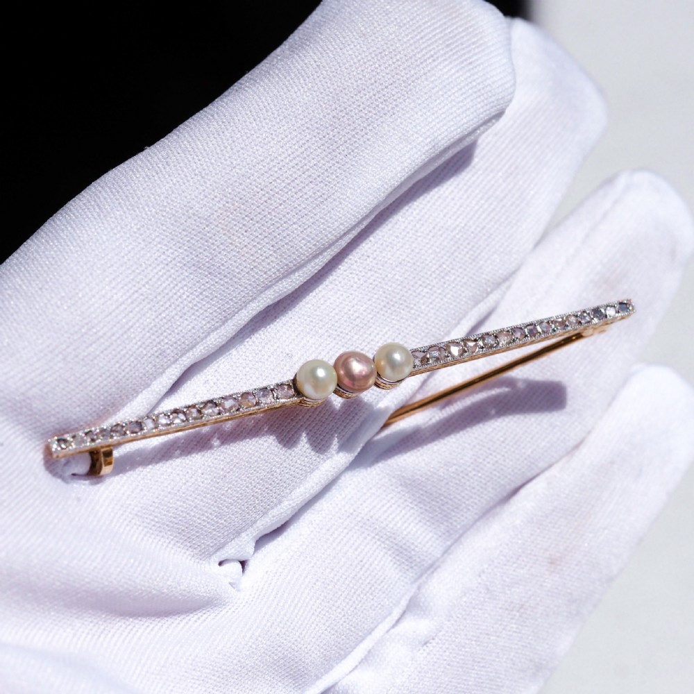 An antique platinum and gold linear bar brooch set with diamonds and three central pearls, featuring a soft pink pearl in the centre. View XI