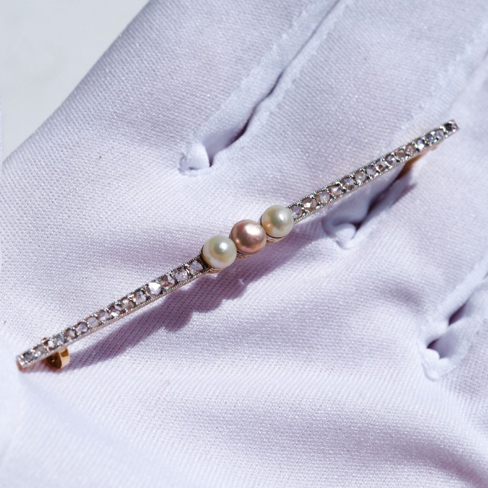 An antique platinum and gold linear bar brooch set with diamonds and three central pearls, featuring a soft pink pearl in the centre. View XII