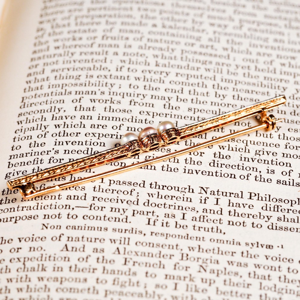 An antique platinum and gold linear bar brooch set with diamonds and three central pearls, featuring a soft pink pearl in the centre. View XIV