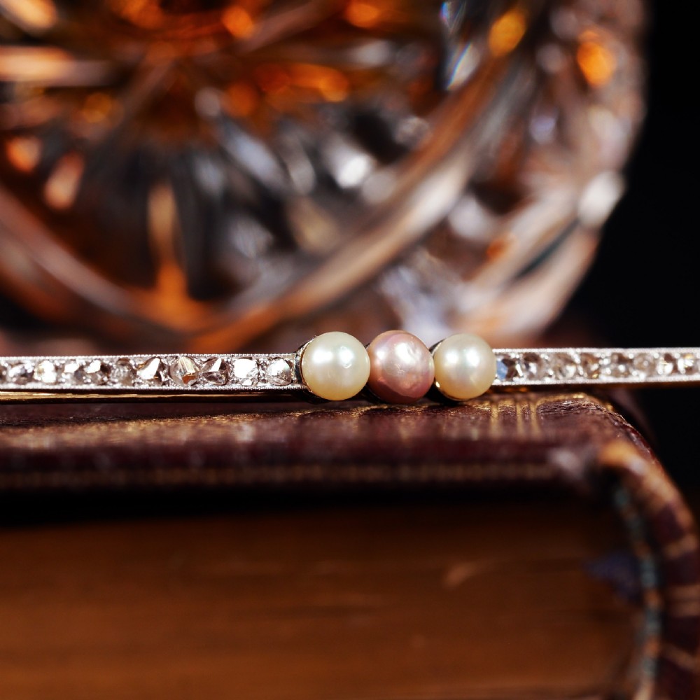 An antique platinum and gold linear bar brooch set with diamonds and three central pearls, featuring a soft pink pearl in the centre. View XVIII