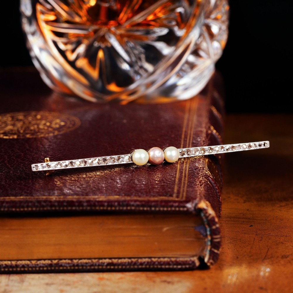 An antique platinum and gold linear bar brooch set with diamonds and three central pearls, featuring a soft pink pearl in the centre. View XIX