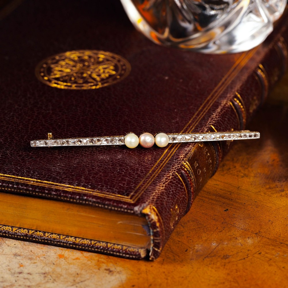 An antique platinum and gold linear bar brooch set with diamonds and three central pearls, featuring a soft pink pearl in the centre. View XX
