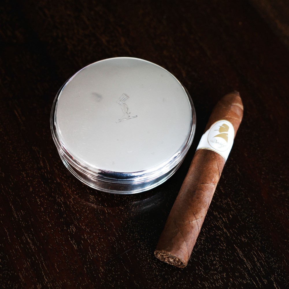 A circular Georgian sterling silver tobacco box featuring a polished flat cover hand-engraved with a crest. View V