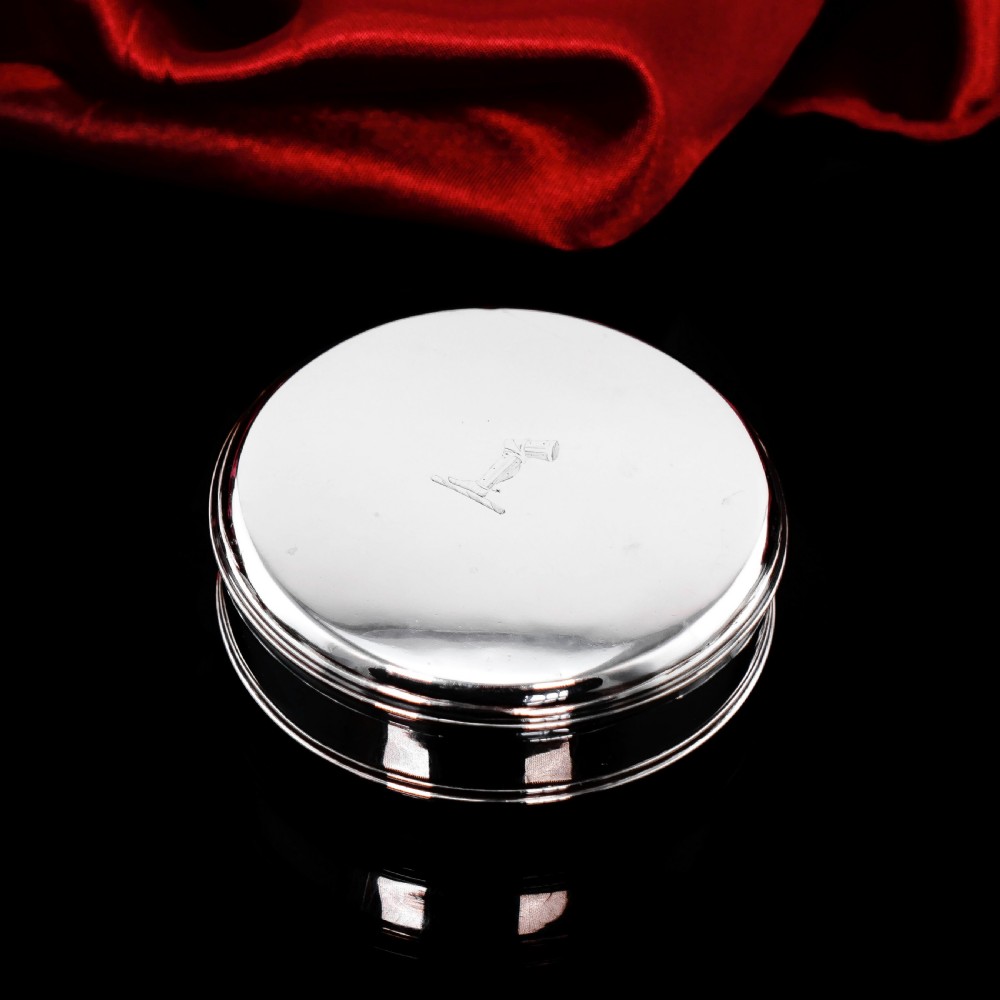 A circular Georgian sterling silver tobacco box featuring a polished flat cover hand-engraved with a crest. View VII