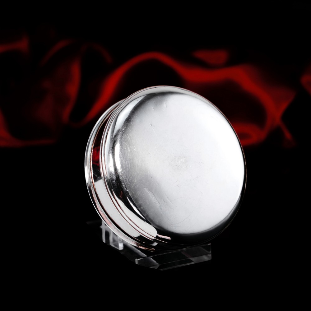 A circular Georgian sterling silver tobacco box featuring a polished flat cover hand-engraved with a crest. View X