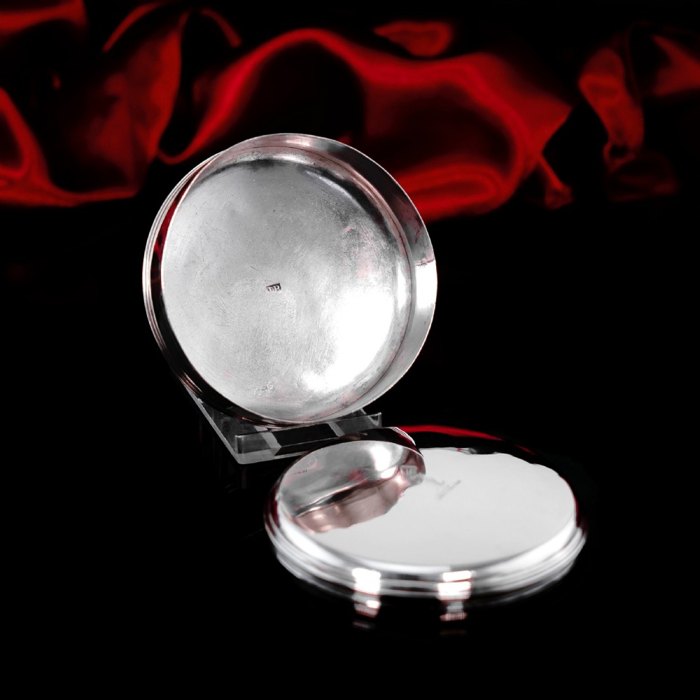 A circular Georgian sterling silver tobacco box featuring a polished flat cover hand-engraved with a crest. View XII