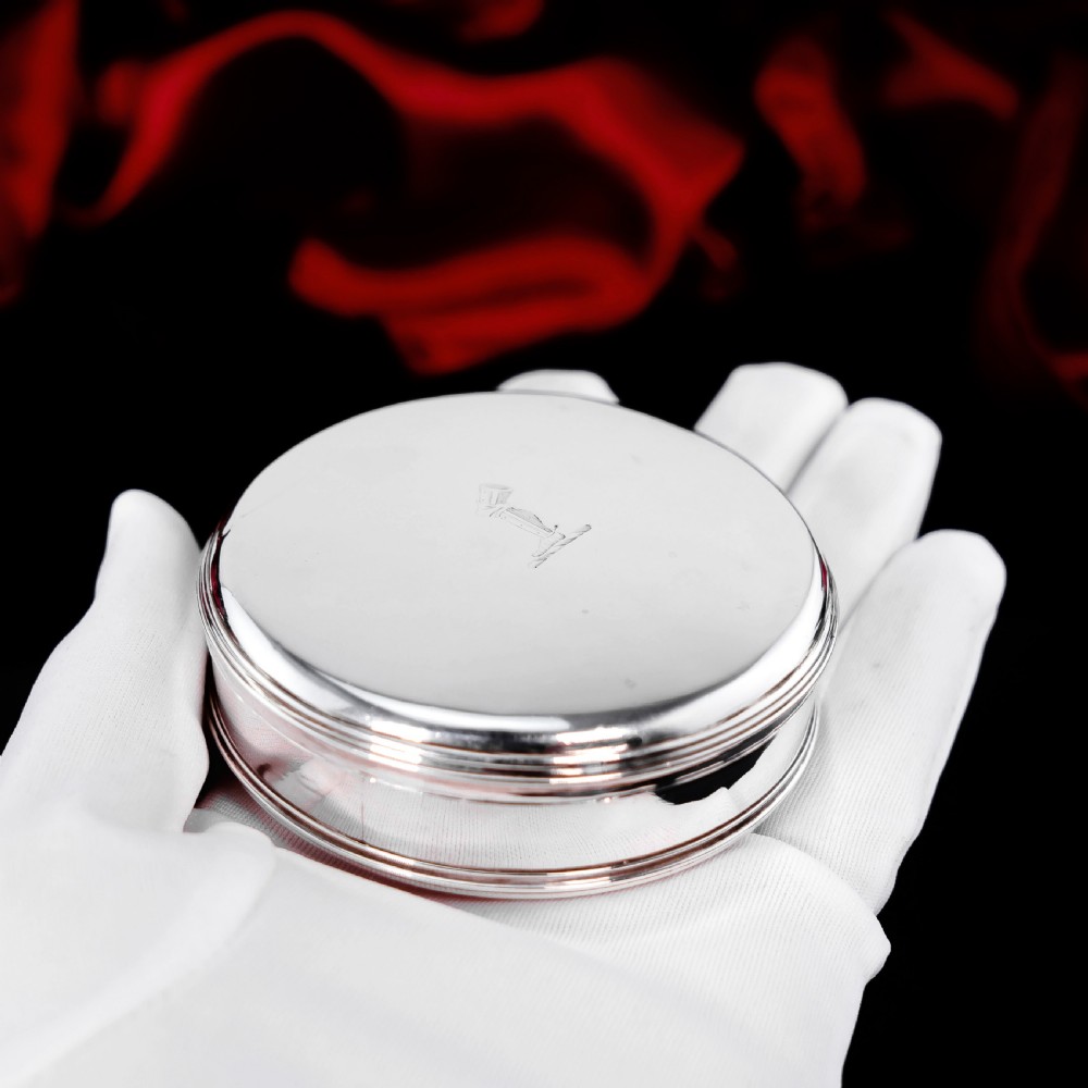A circular Georgian sterling silver tobacco box featuring a polished flat cover hand-engraved with a crest. View XV