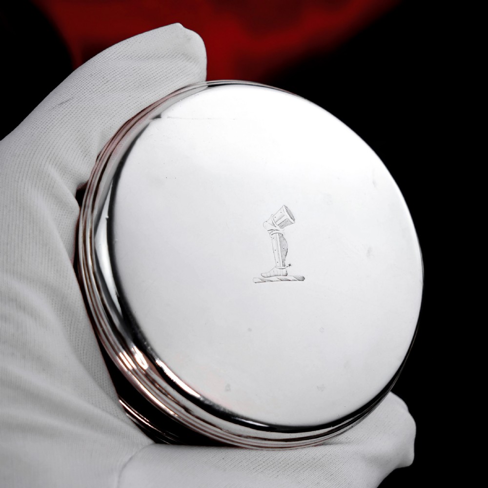 A circular Georgian sterling silver tobacco box featuring a polished flat cover hand-engraved with a crest. View XVI