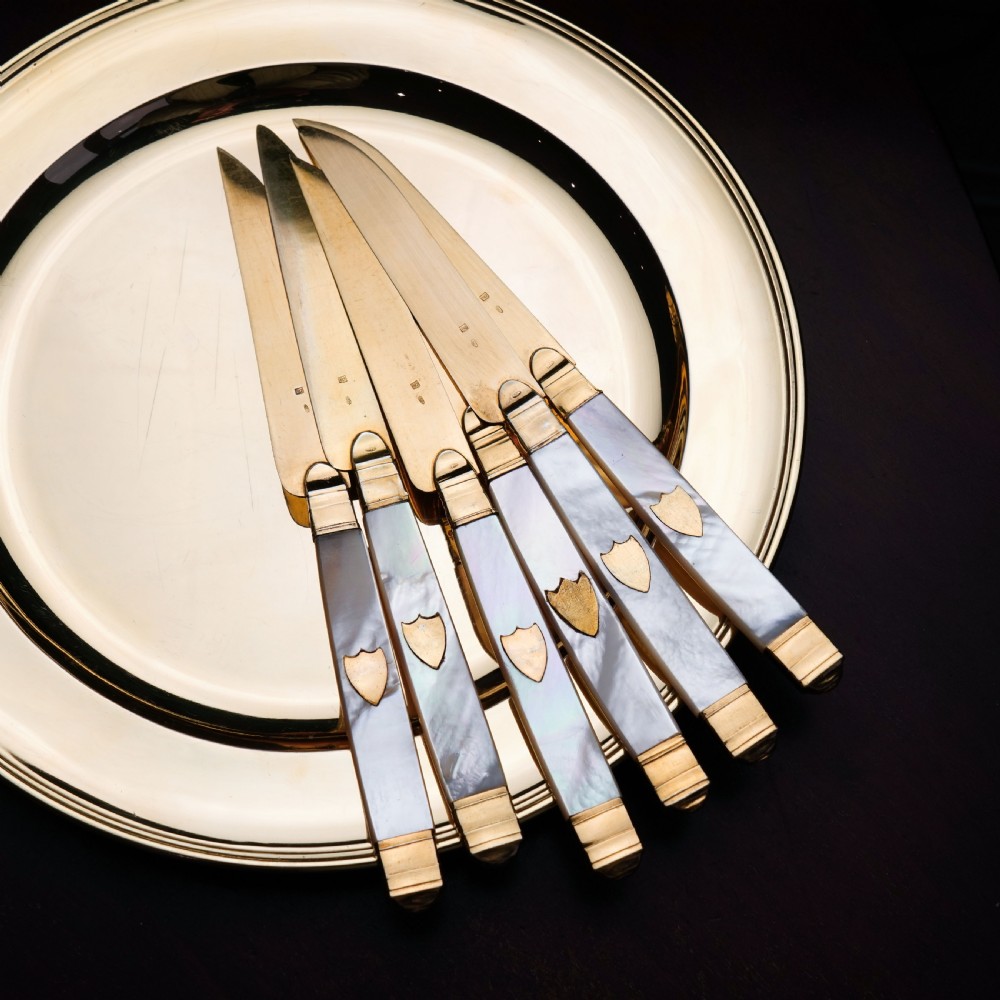 A set of six 19th-century fruit knives featuring silver-gilt blades and mother-of-pearl handles inlaid with small shield motifs. View II