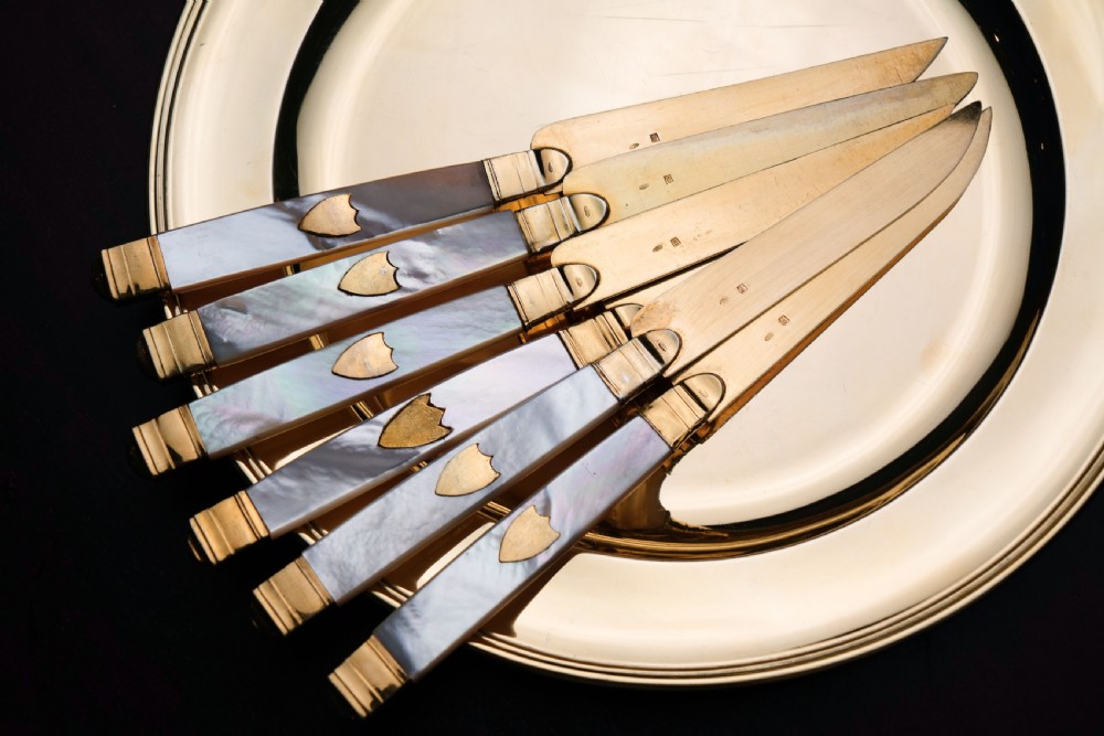 A set of six 19th-century fruit knives featuring silver-gilt blades and mother-of-pearl handles inlaid with small shield motifs. View IV