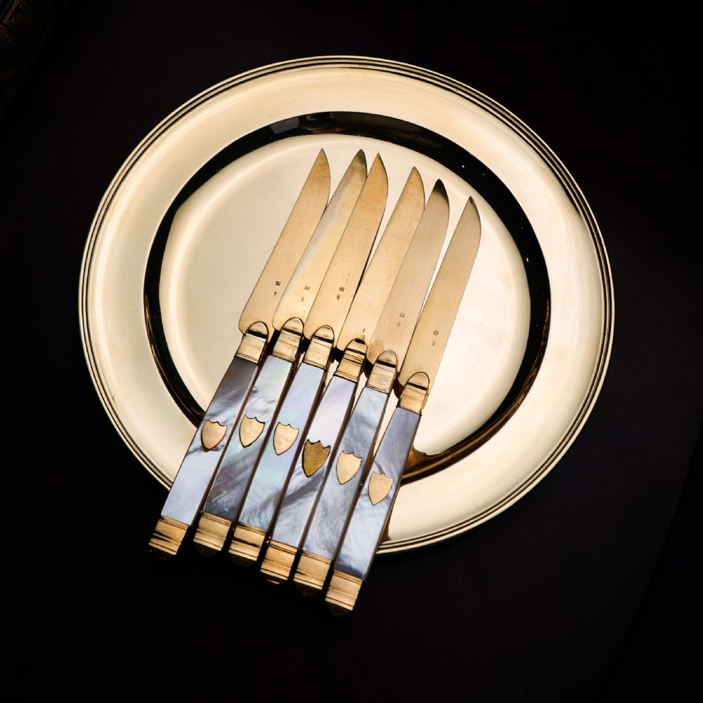 A set of six 19th-century fruit knives featuring silver-gilt blades and mother-of-pearl handles inlaid with small shield motifs. View V