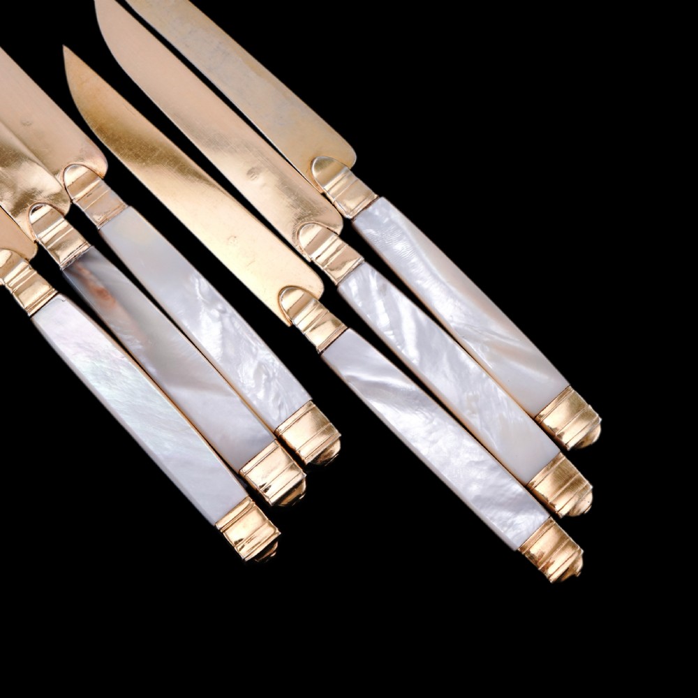 A set of six 19th-century fruit knives featuring silver-gilt blades and mother-of-pearl handles inlaid with small shield motifs. View XXIV