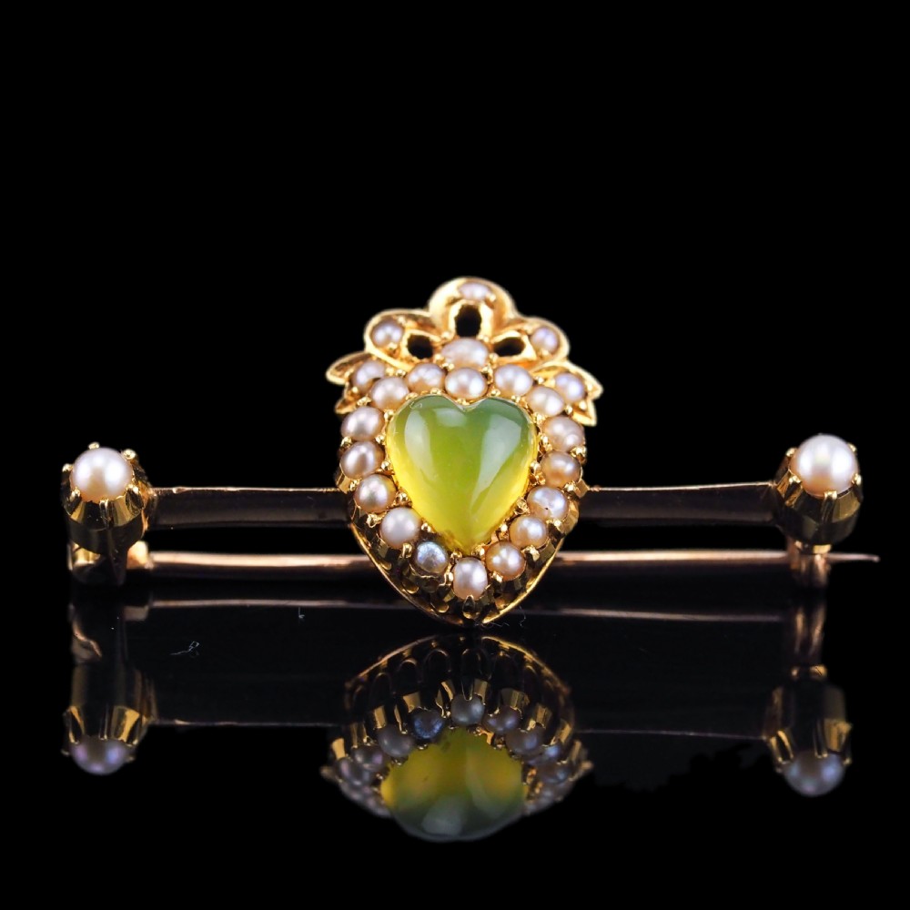 A late Victorian 15ct gold bar brooch featuring a central heart-shaped green chalcedony cabochon framed by seed pearls.