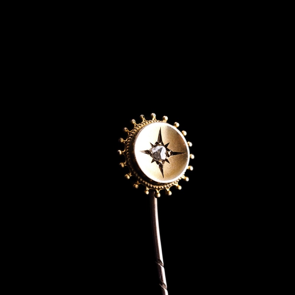 A Victorian 14ct gold stick pin featuring a round head with a star-set diamond and a beaded granulated outer border. View V