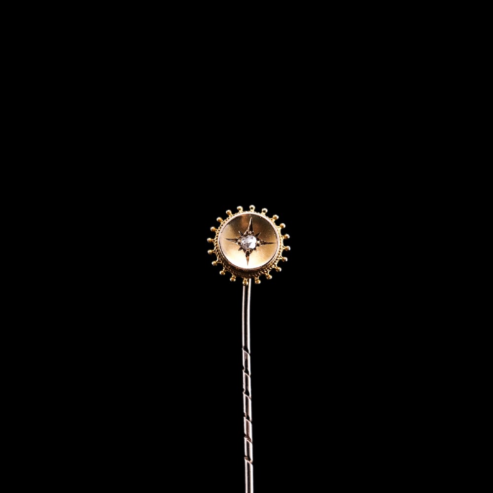 A Victorian 14ct gold stick pin featuring a round head with a star-set diamond and a beaded granulated outer border. View X