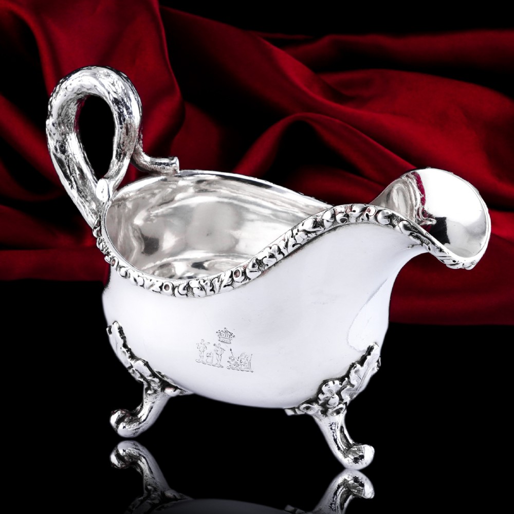 A Victorian sterling silver sauce boat featuring an organic twig handle, acorn feet, and engraved crest detailing.